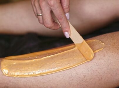 hands make depilation procedure on woman legs with wax